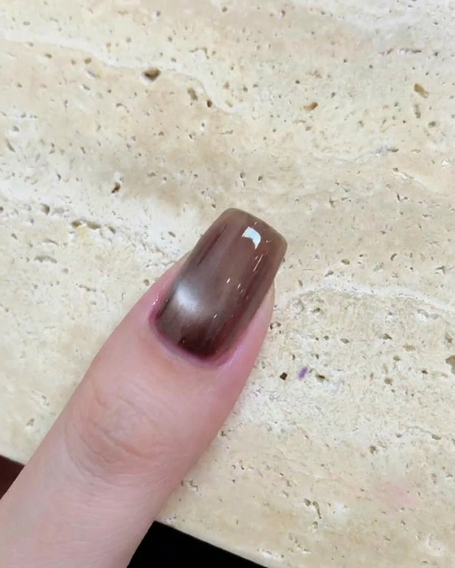 Primer plano de una uña marrón brillante con un efecto cat eye circular y reflectante después de ser curada.