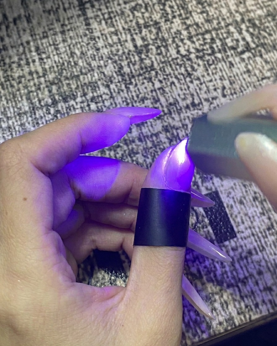 Un dedo dentro de una lámpara portátil de uñas UV/LED con la luz encendida.