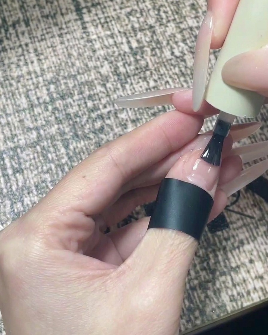 Un pincel aplicando top coat transparente y brillante en un diseño de uñas terminado con estrellas negras.