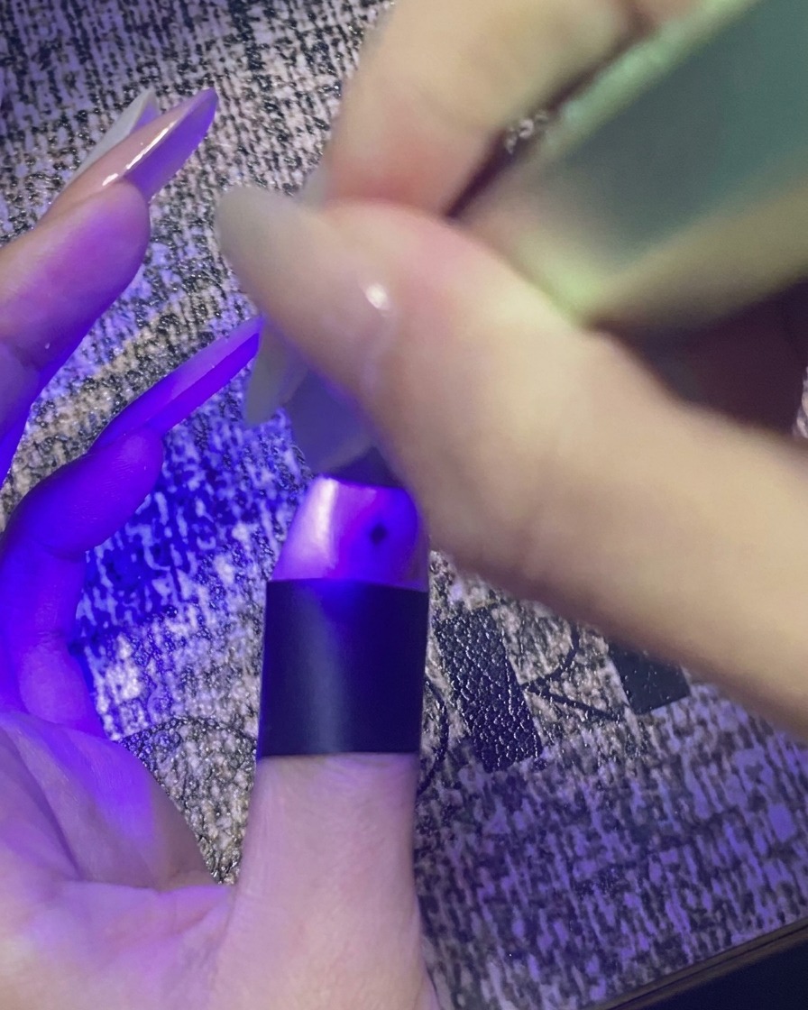 Un pulgar con diseño de estrellas curándose bajo una pequeña luz UV/LED morada.