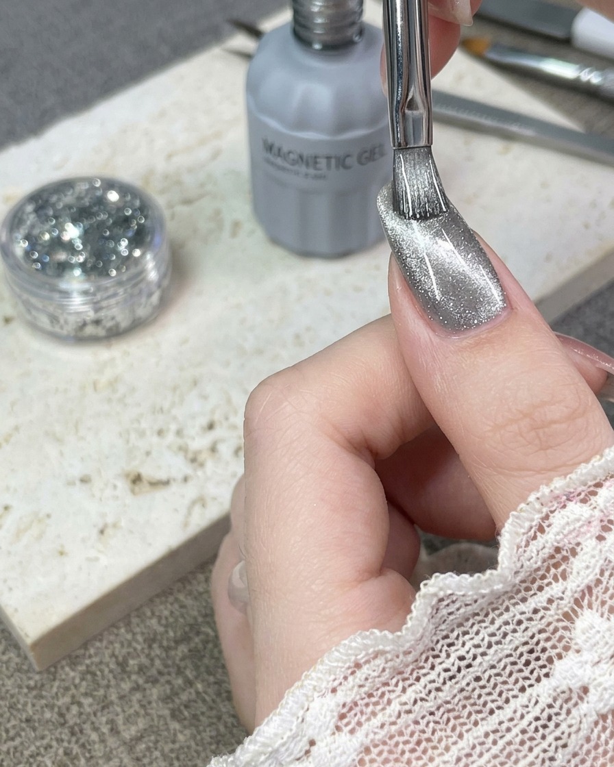 Un pincel aplicando una capa de esmalte en gel ojo de gato plateado sobre una uña natural.