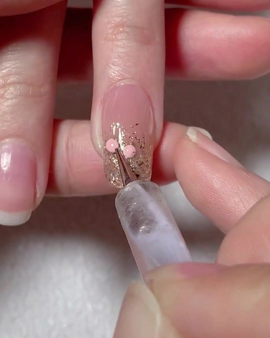 Una herramienta de puntos colocando dos puntos de gel rosa sobre la superficie de la uña para marcar el diseño de un corazón.