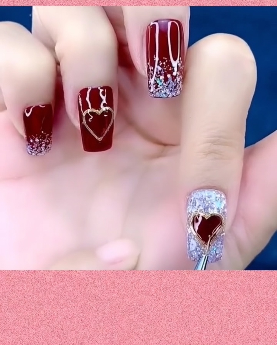 Un pincel de arte en uñas aplicando top coat alrededor de los bordes de un dije de corazón metálico en una uña.