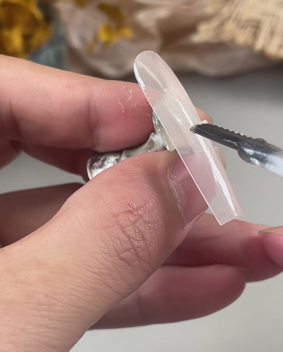 Una mano utilizando una herramienta para colocar partículas de purpurina holográfica iridiscente sobre el gel húmedo y sin curar.