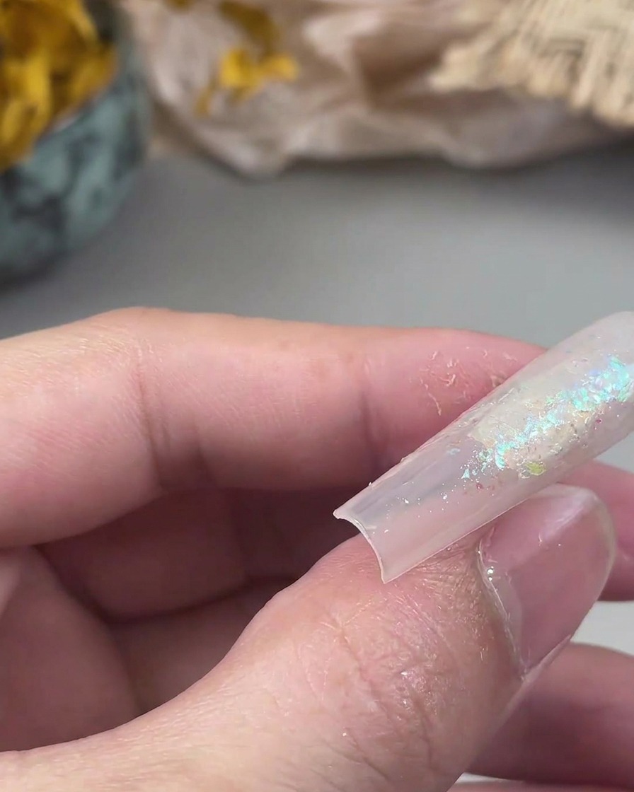 Un pincel plano pequeño presionando partículas de purpurina sobre una superficie de gel pegajosa en una uña.