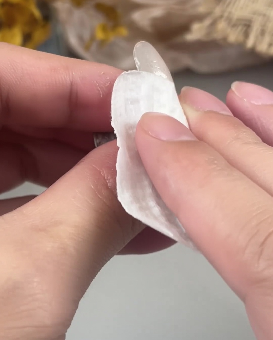 Una mano utilizando una toallita sin pelusa para limpiar la superficie de una uña de gel curada.