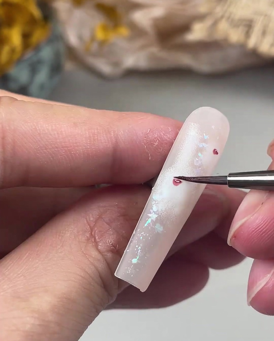 Un pincel fino para detalles pintando pétalos pequeños y delicados de color rosa oscuro alrededor de un corazón central.