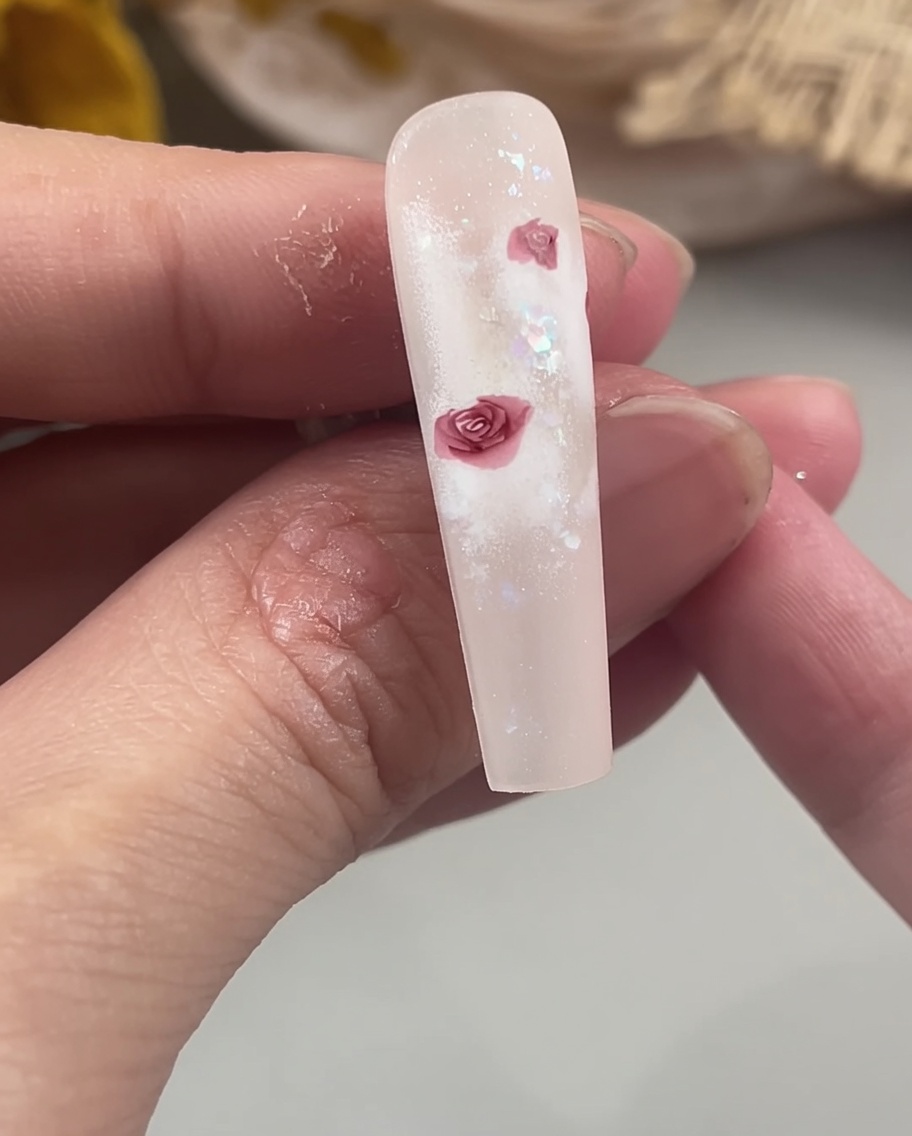 Un pincel de detalle rellenando los centros de los pétalos de rosa en una uña para crear una forma floral sólida y definida.