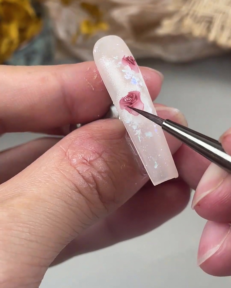 Un pincel de detalle añadiendo pétalos delicados que se curvan hacia afuera en el borde de un diseño de rosa.