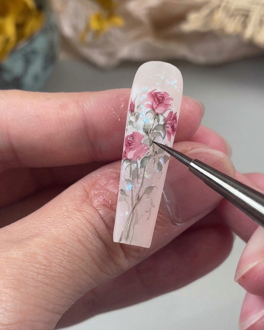 Un pincel de detalle fino dibujando tallos curvos y orgánicos en un tono verde suave, conectando elementos florales en la uña.