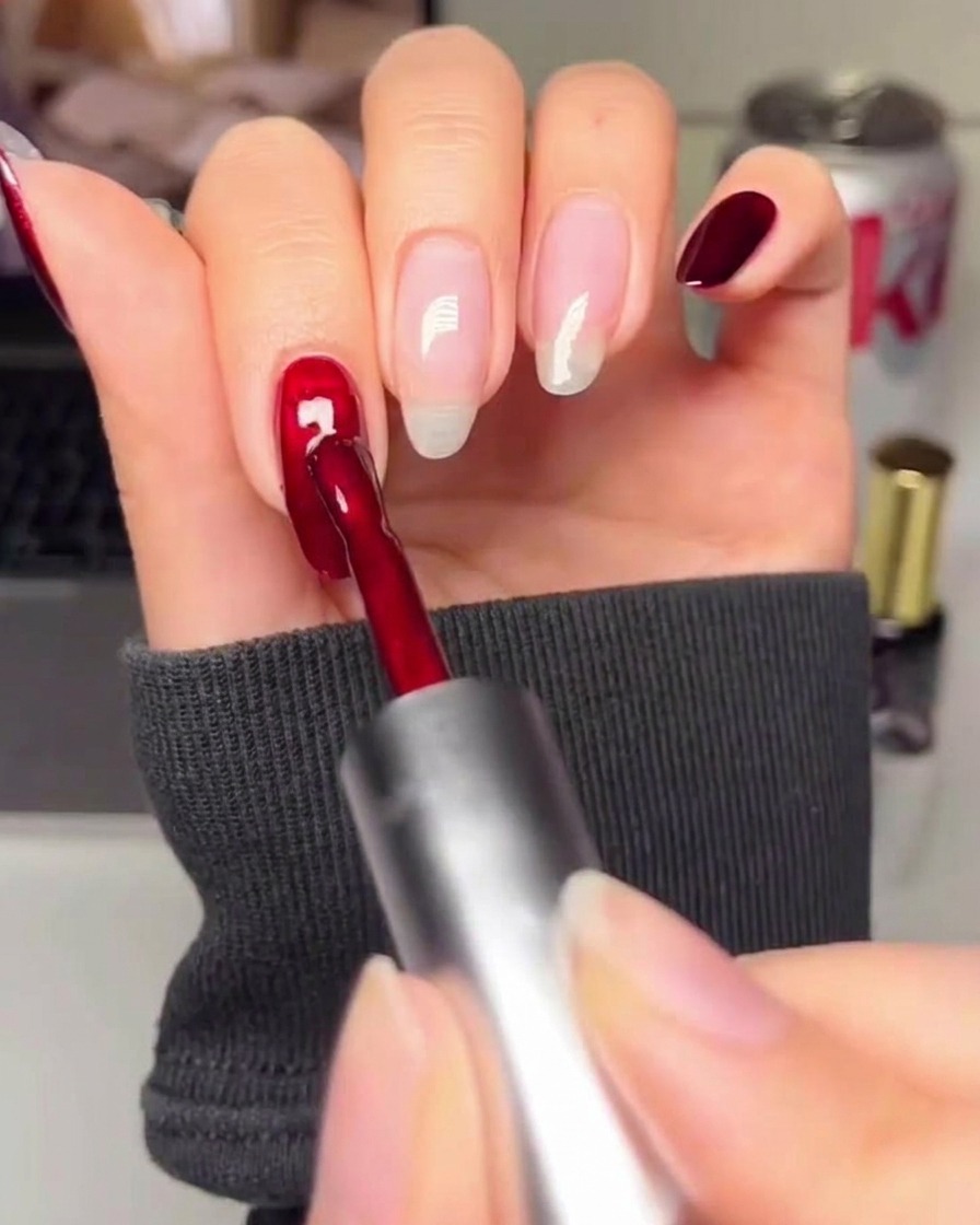 Primer plano de un pincel de uñas aplicando un esmalte en gel rojo profundo y rico sobre una superficie de uña preparada.