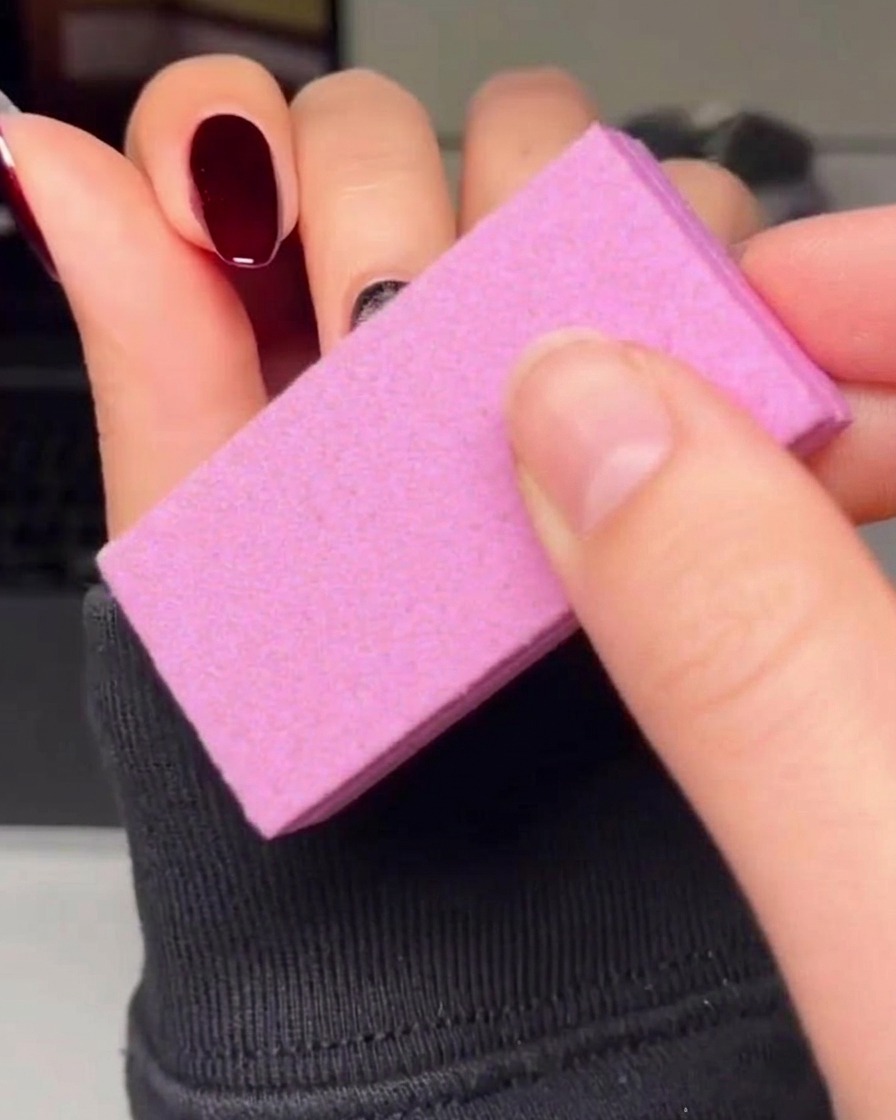 Un pincel delineador fino trazando cuidadosamente el perímetro de un corazón rojo sobre una uña con esmalte en gel negro.