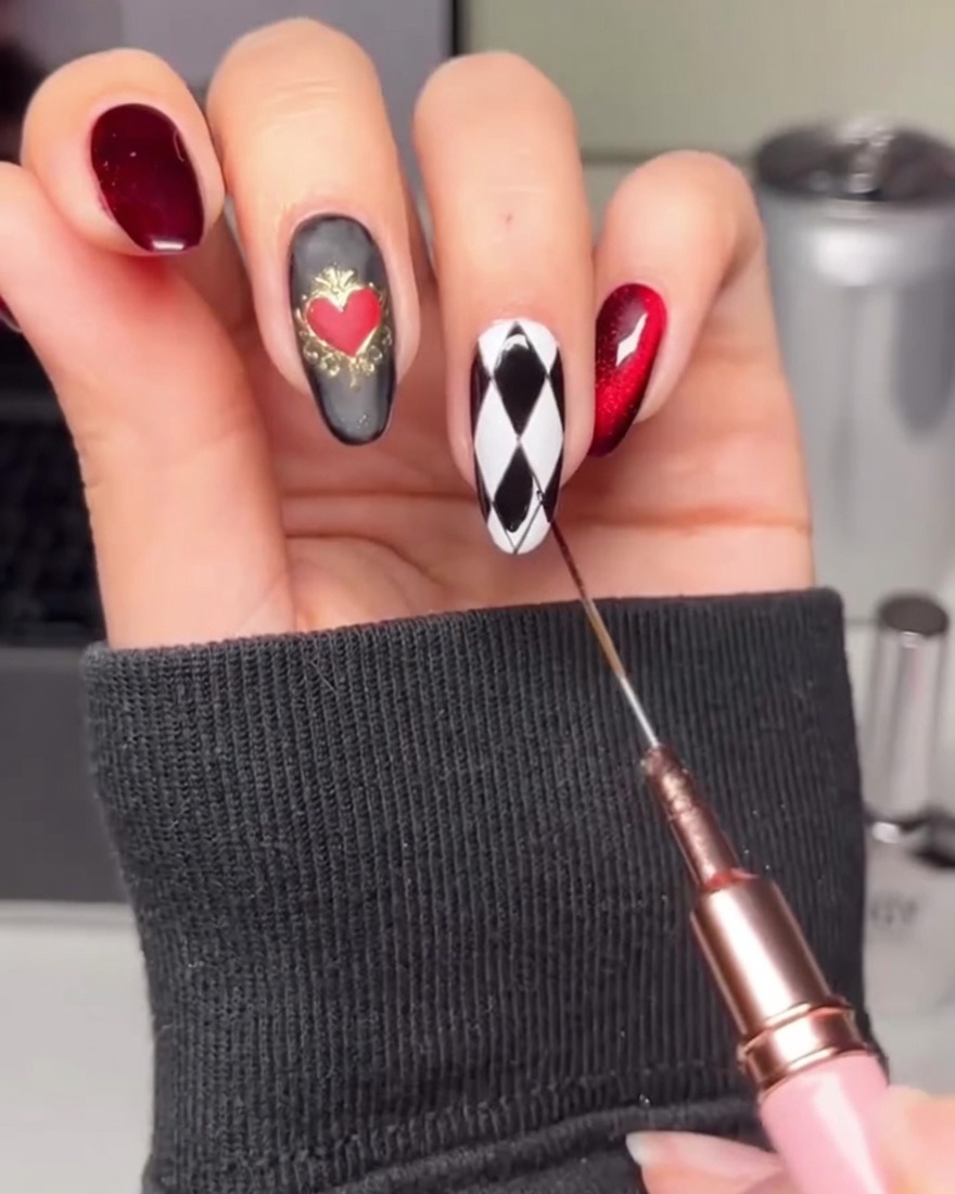 Una mano usando un pincel delineador para rellenar formas de diamante alternas en una uña blanca con gel negro.