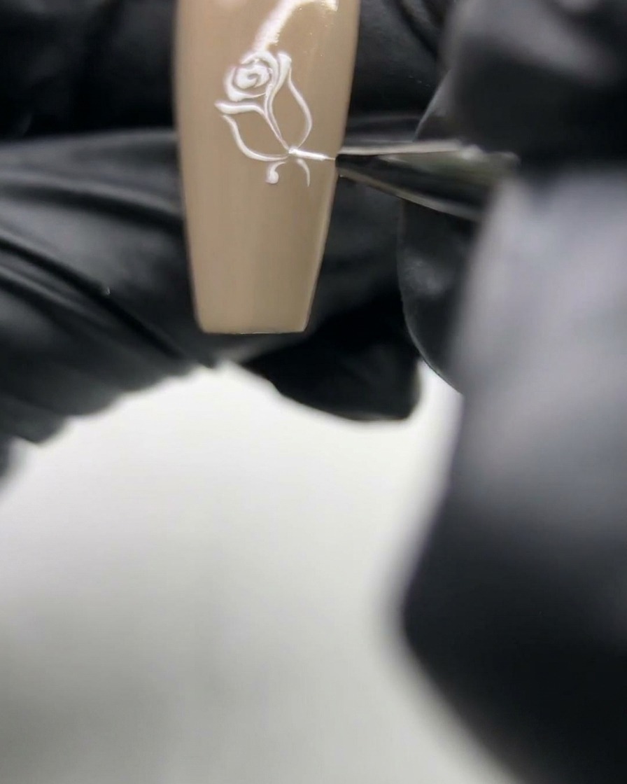 Primer plano de un pincel de uñas añadiendo un detalle delicado de hoja al lado de un tallo de rosa pintado.