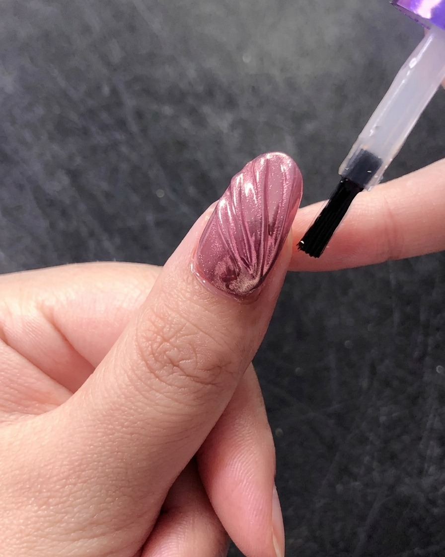 Un pincel aplicando un top coat final brillante sobre un diseño de uña de concha cromada.