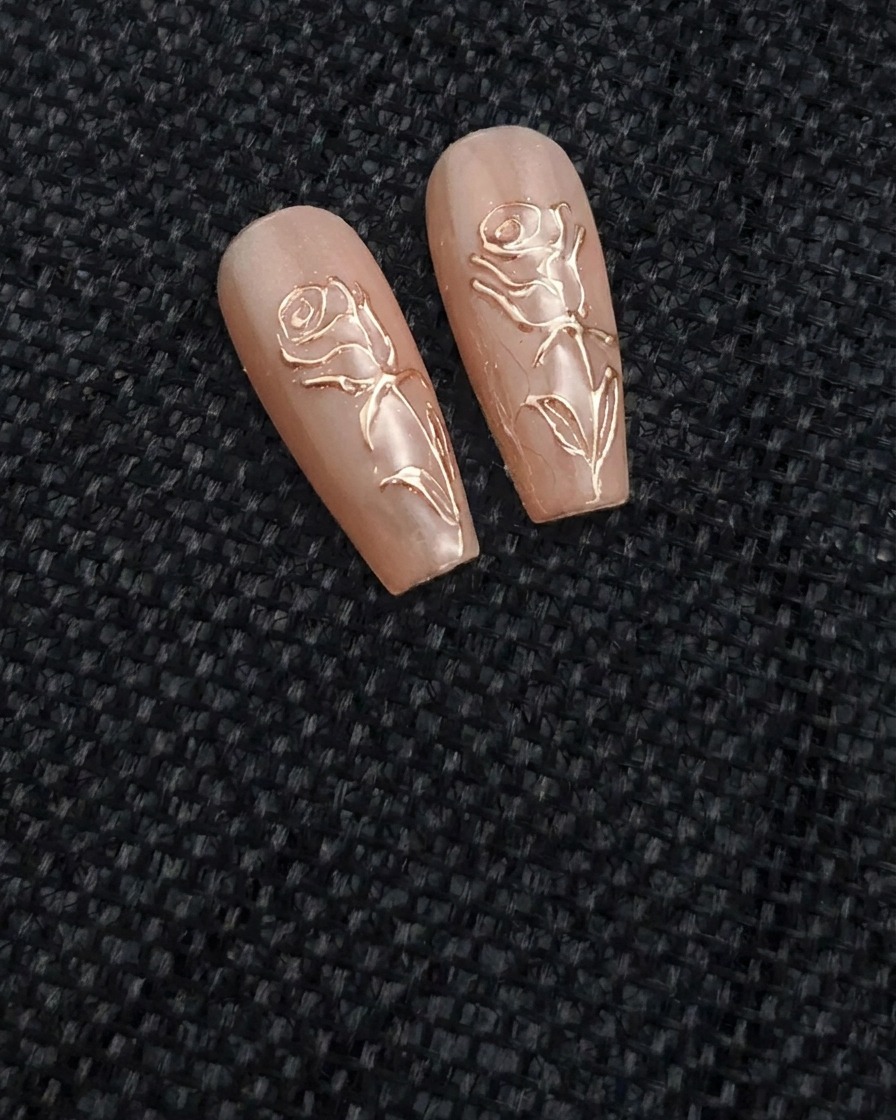 Un pincel fino de nail art aplicando una línea de gel transparente en relieve con forma de rosa sobre una uña de color nude.