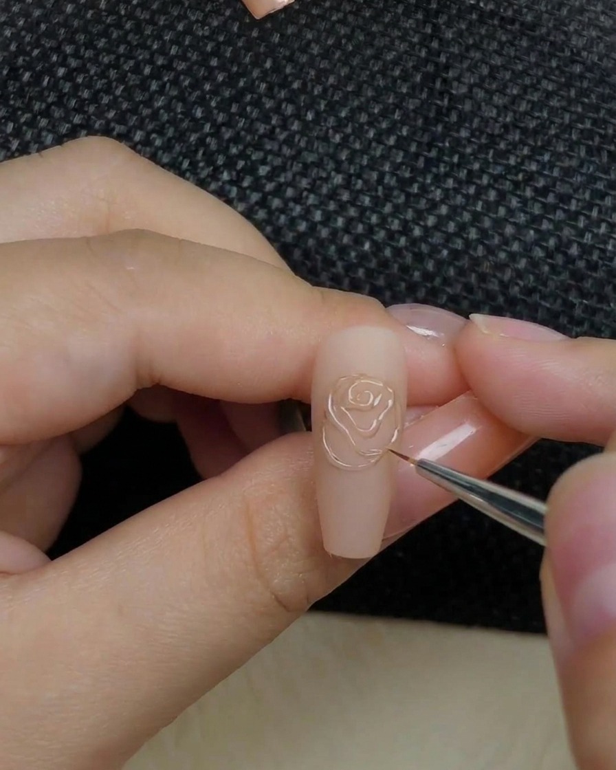 Un primer plano de una mano colocando una uña con un diseño de rosa en relieve dentro de una lámpara de curado.