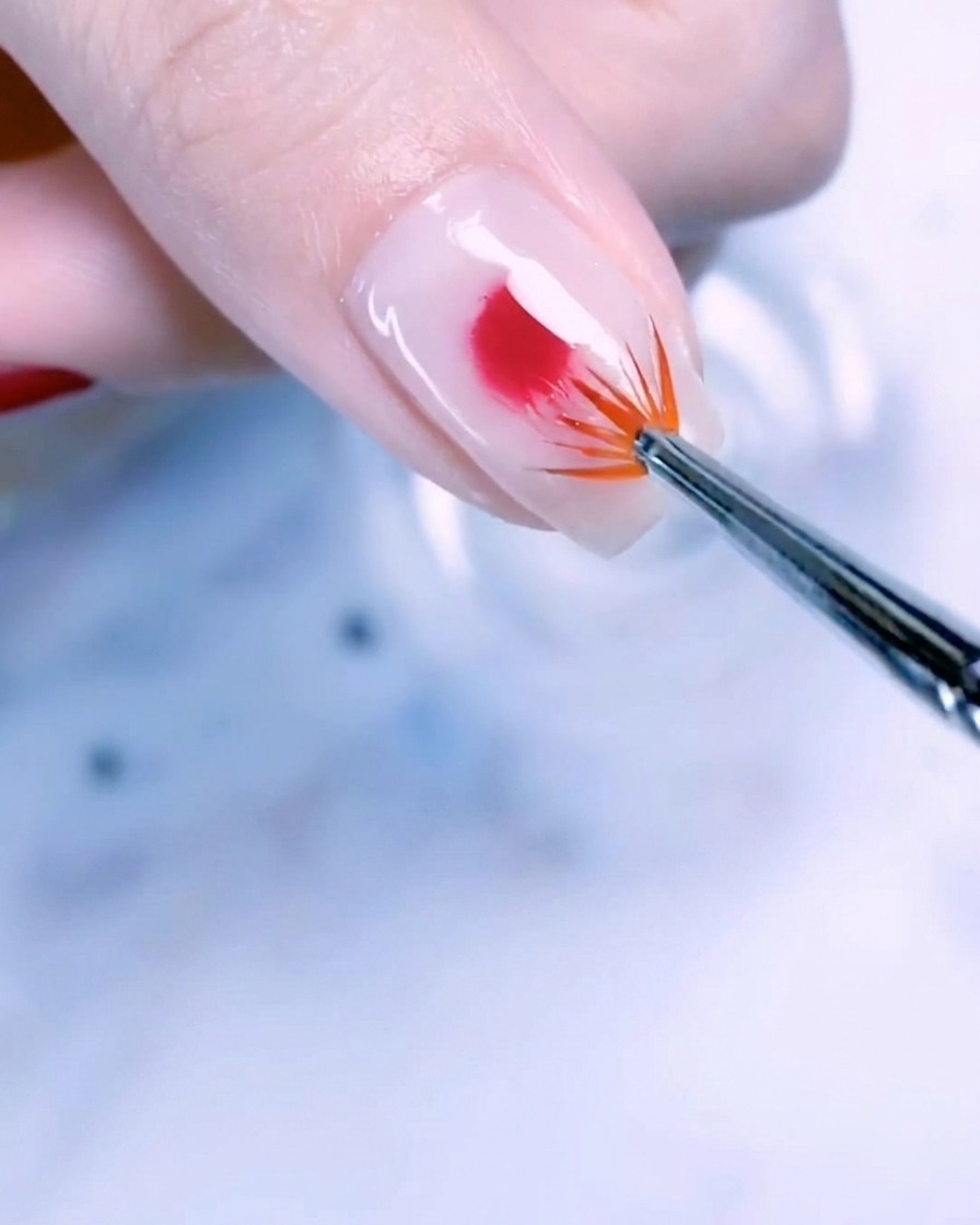 Primer plano de la uña del pulgar con una base blanco lechoso y una gota centrada de gel oro rosa difuminándose hacia fuera con un pincel abanico.