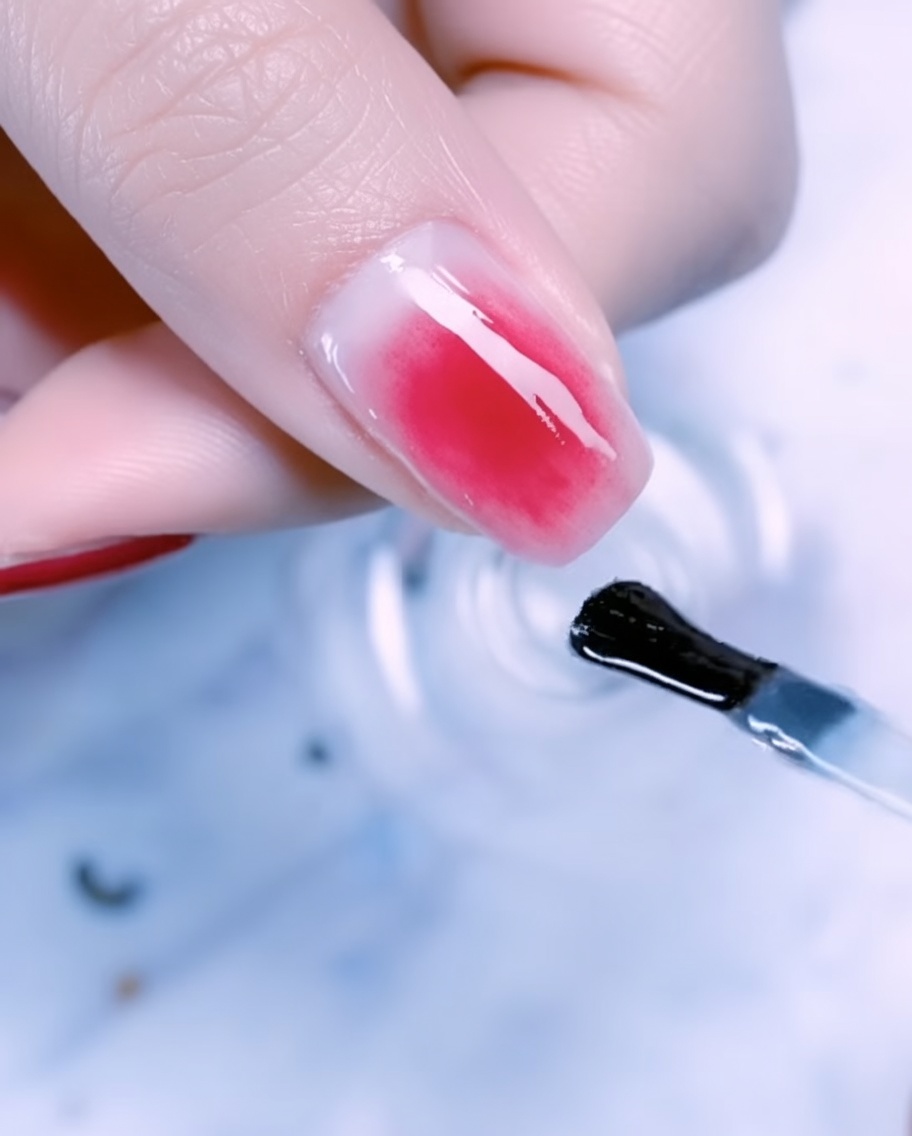Primer plano de la uña de un pulgar decorada con pan de oro, finos detalles de hilo metálico y perlas sobre un degradado oro rosa.