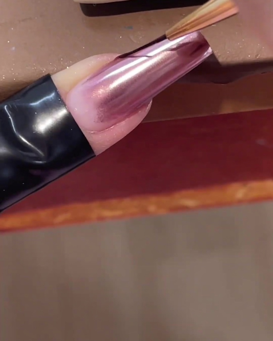 Un pincel delineador de arte de uñas aplicando una línea transparente de gel constructor diagonalmente a través de una uña cromada.