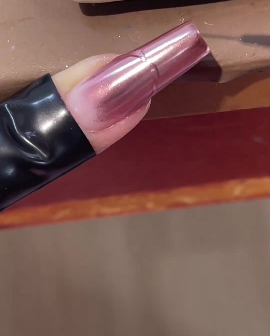Un pincel delineador fino dibujando una línea de gel transparente elevada sobre una uña cromo rosa.