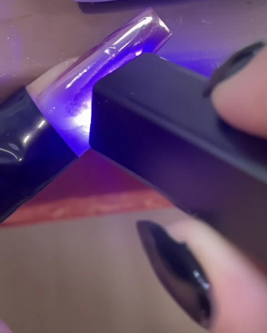 Una mini lámpara UV/LED de mano curando líneas de gel constructor 3D transparentes en una extensión de uña.