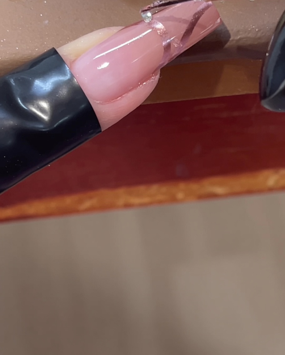 Colocando un pequeño cristal transparente sobre una línea de cromo 3D en una uña rosa usando una herramienta.