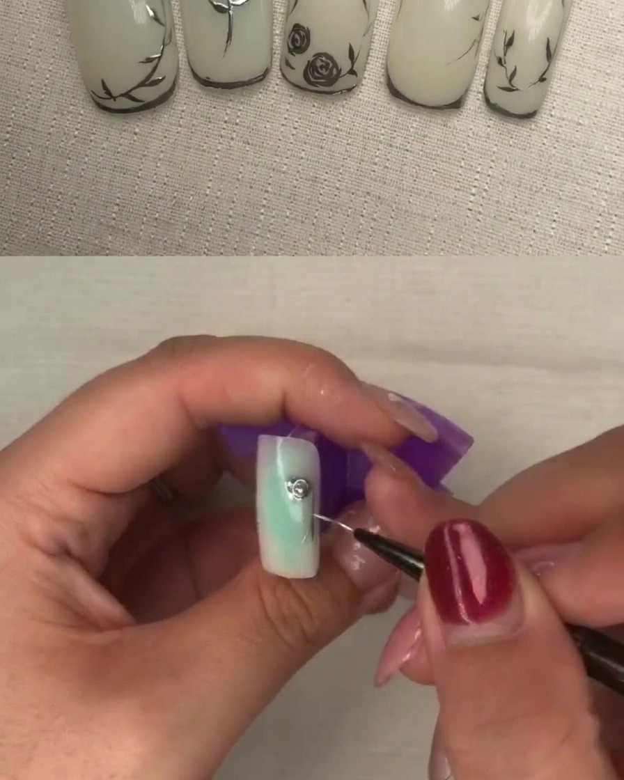 Un primer plano de un pincel liner aplicando gel metálico espeso en el centro de un diseño de pétalos sobre una uña blanca.