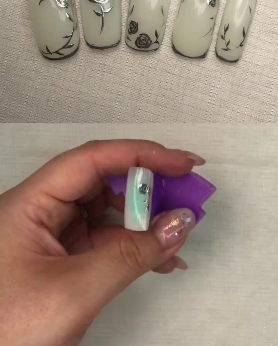 Una vista de cerca del diseño final de pétalos de rosa metálicos en una uña blanca, mostrando una textura detallada.