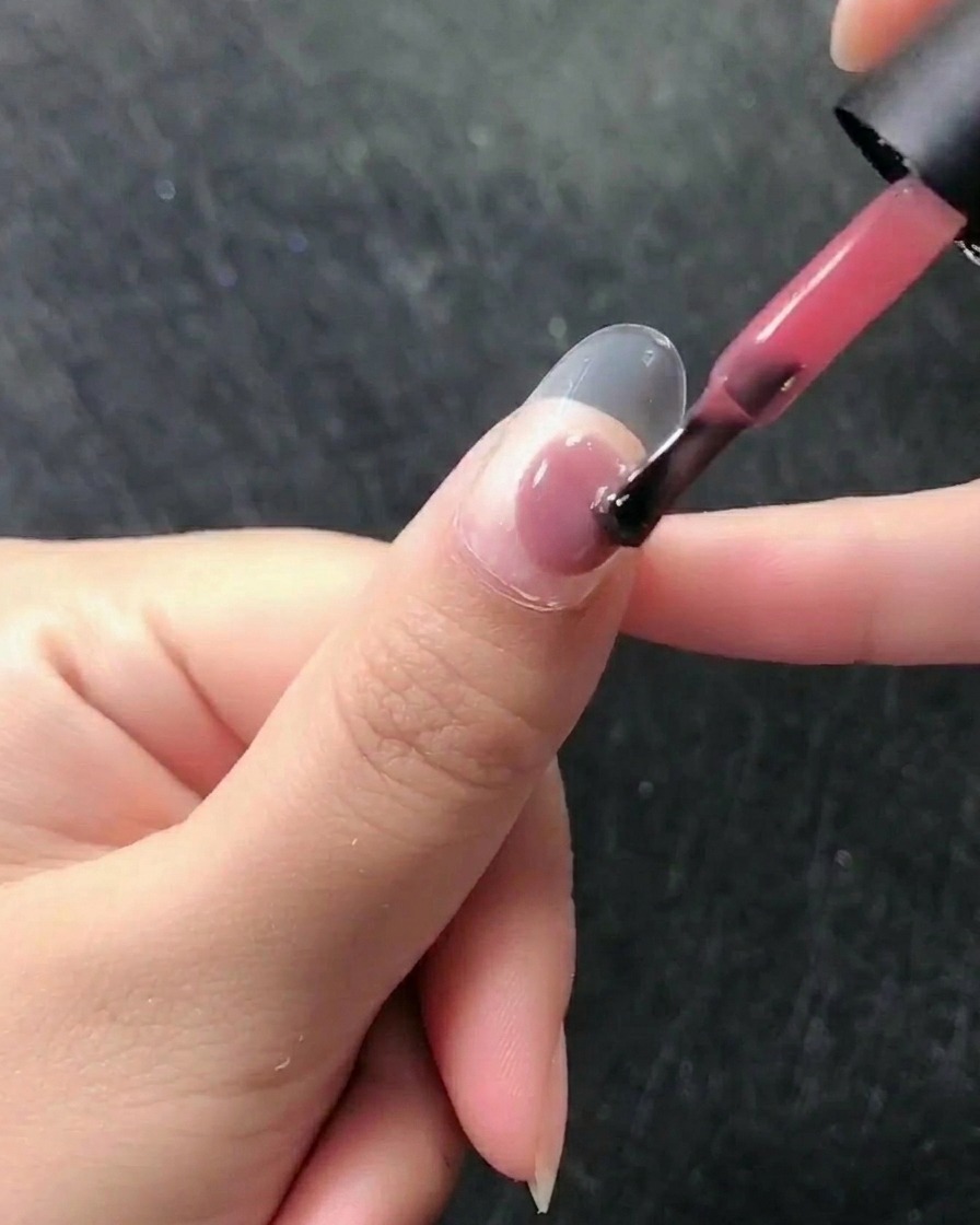 Primer plano de un pincel aplicando esmalte en gel rosa translúcido sobre una uña natural preparada.