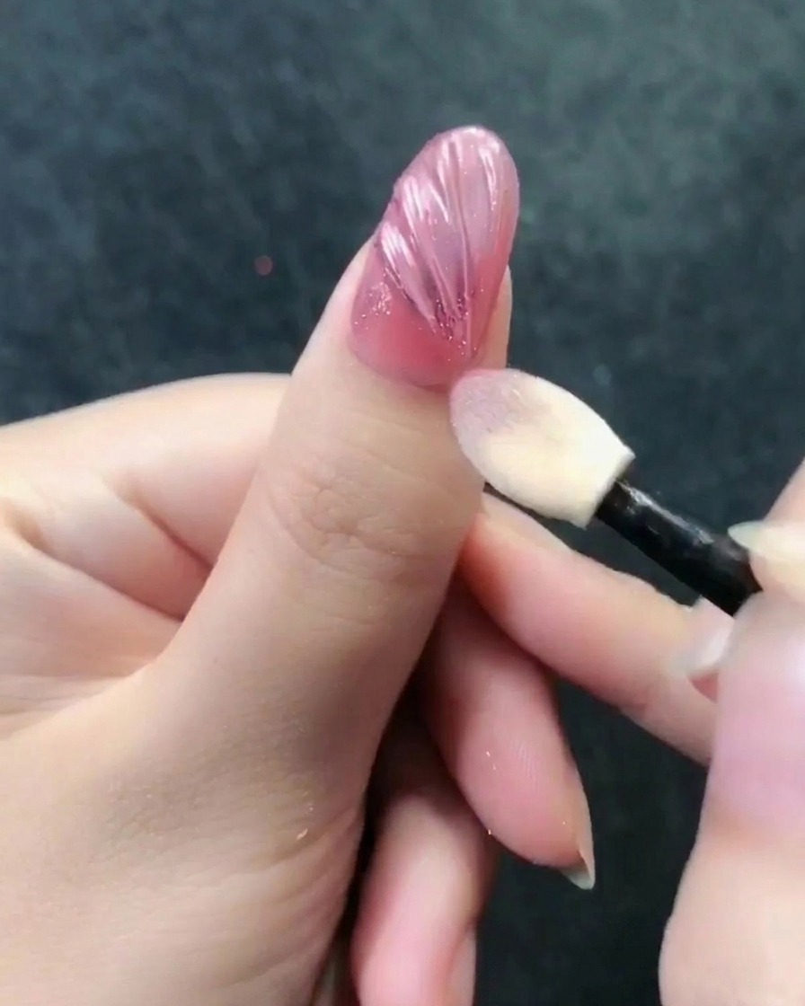 Aplicador de sombras puliendo el polvo cromado oro rosa sobre una superficie de uña texturizada.