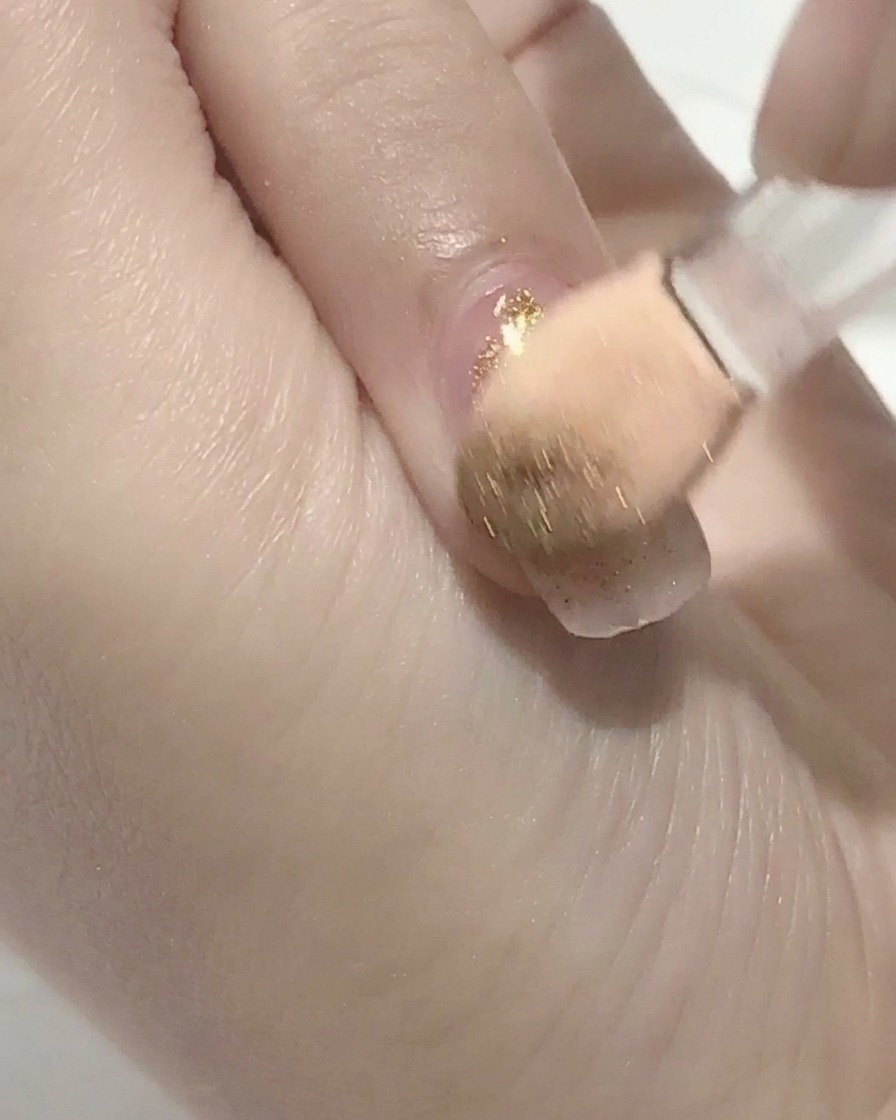 Un pincel aplicando top coat transparente sobre una uña de gel rosa.
