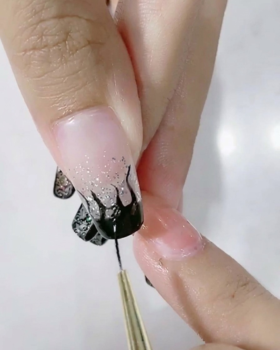 Un pincel liner rellenando el diseño de llamas negras en una uña con degradado.