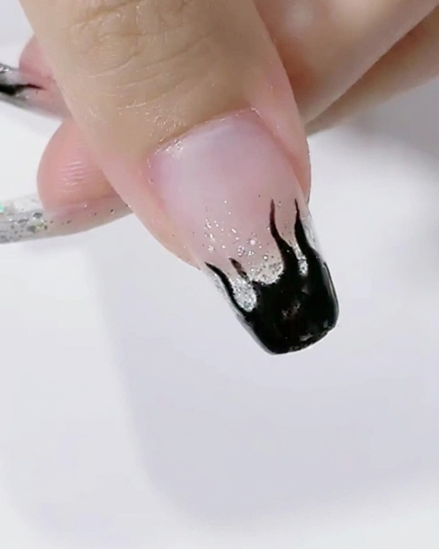 Uñas con diseño de llamas negras curándose bajo la luz de una lámpara LED.