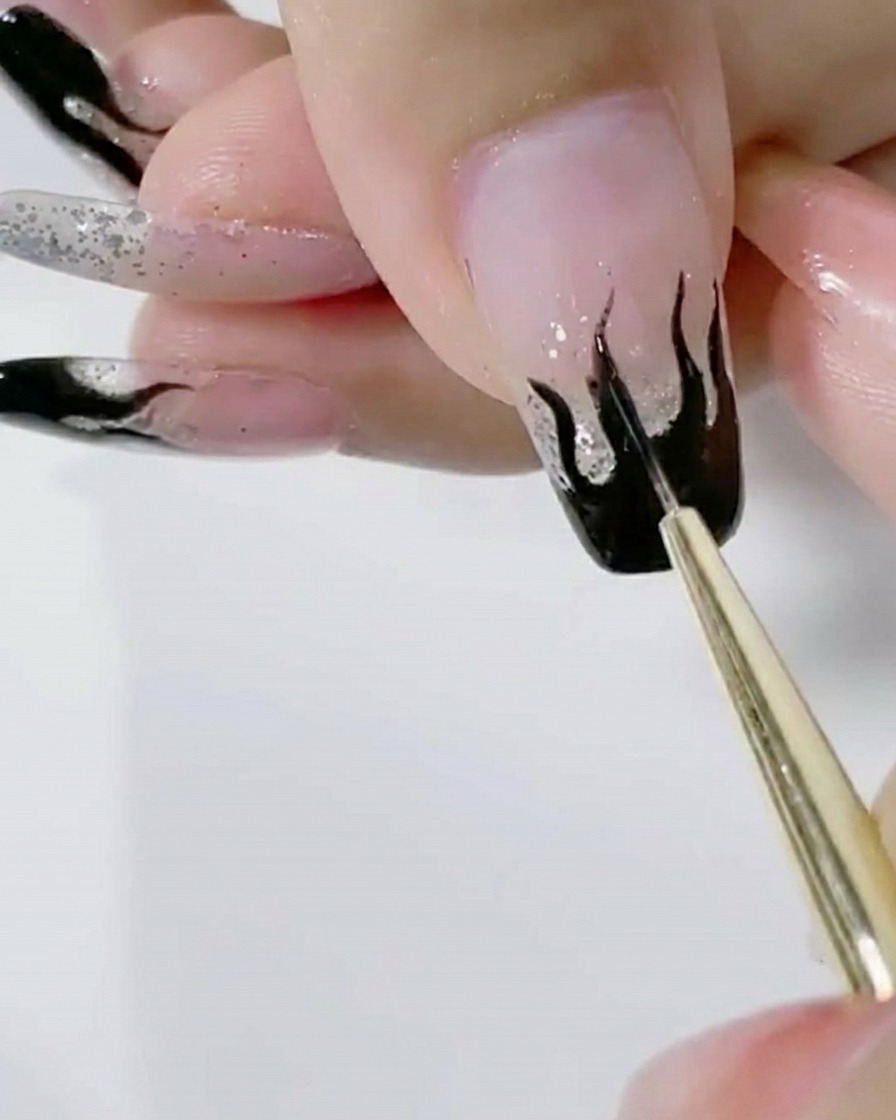 Un pincel liner aplicando una segunda capa de gel negro sobre el diseño de llamas.