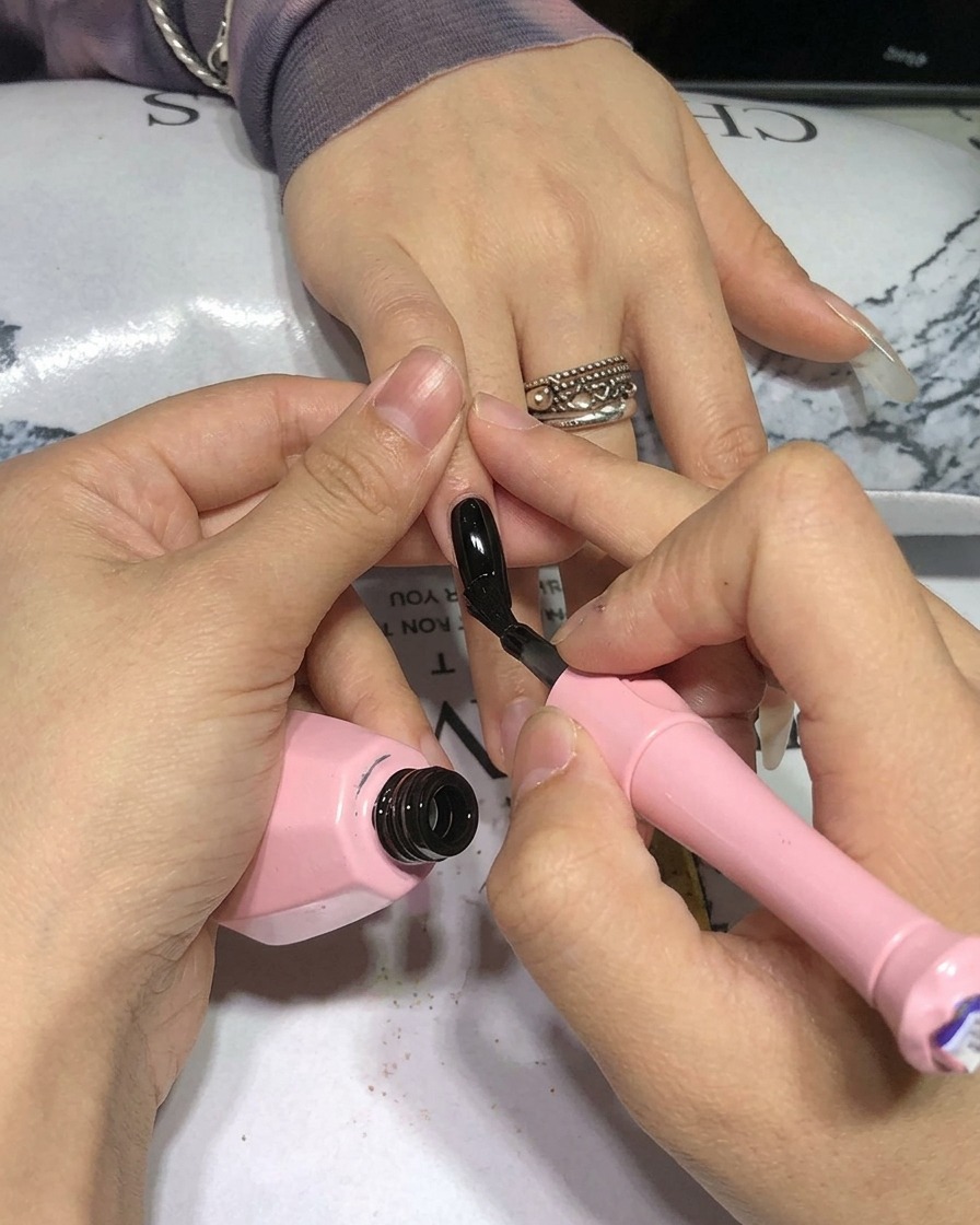 Primer plano de un pincel aplicando esmalte de gel negro sobre una uña natural.
