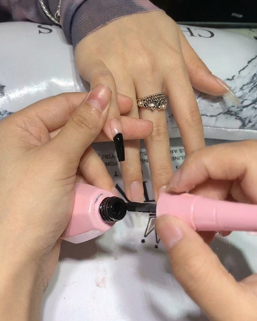 Un pincel aplicando una segunda capa de esmalte de gel negro en la uña, mostrando una saturación profunda.