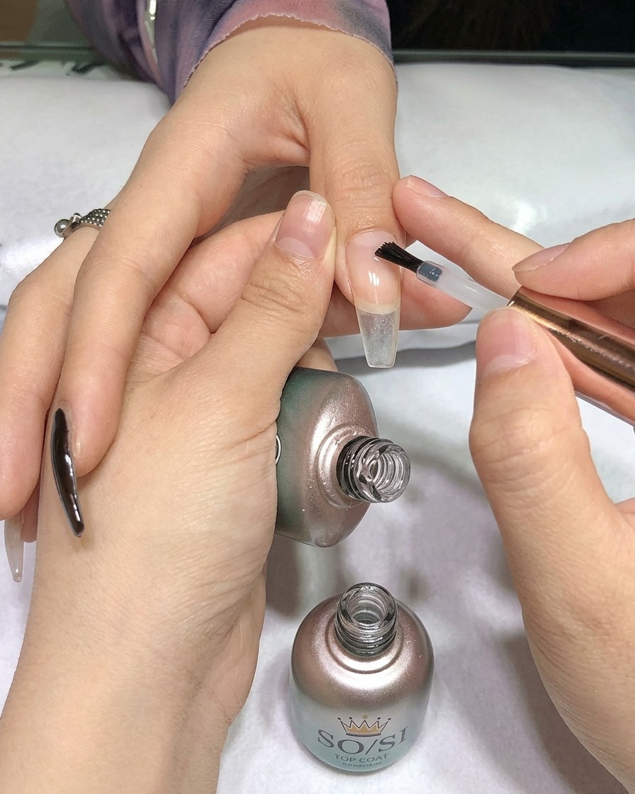 Un pincel aplicando un top coat transparente sobre una uña pintada de negro.