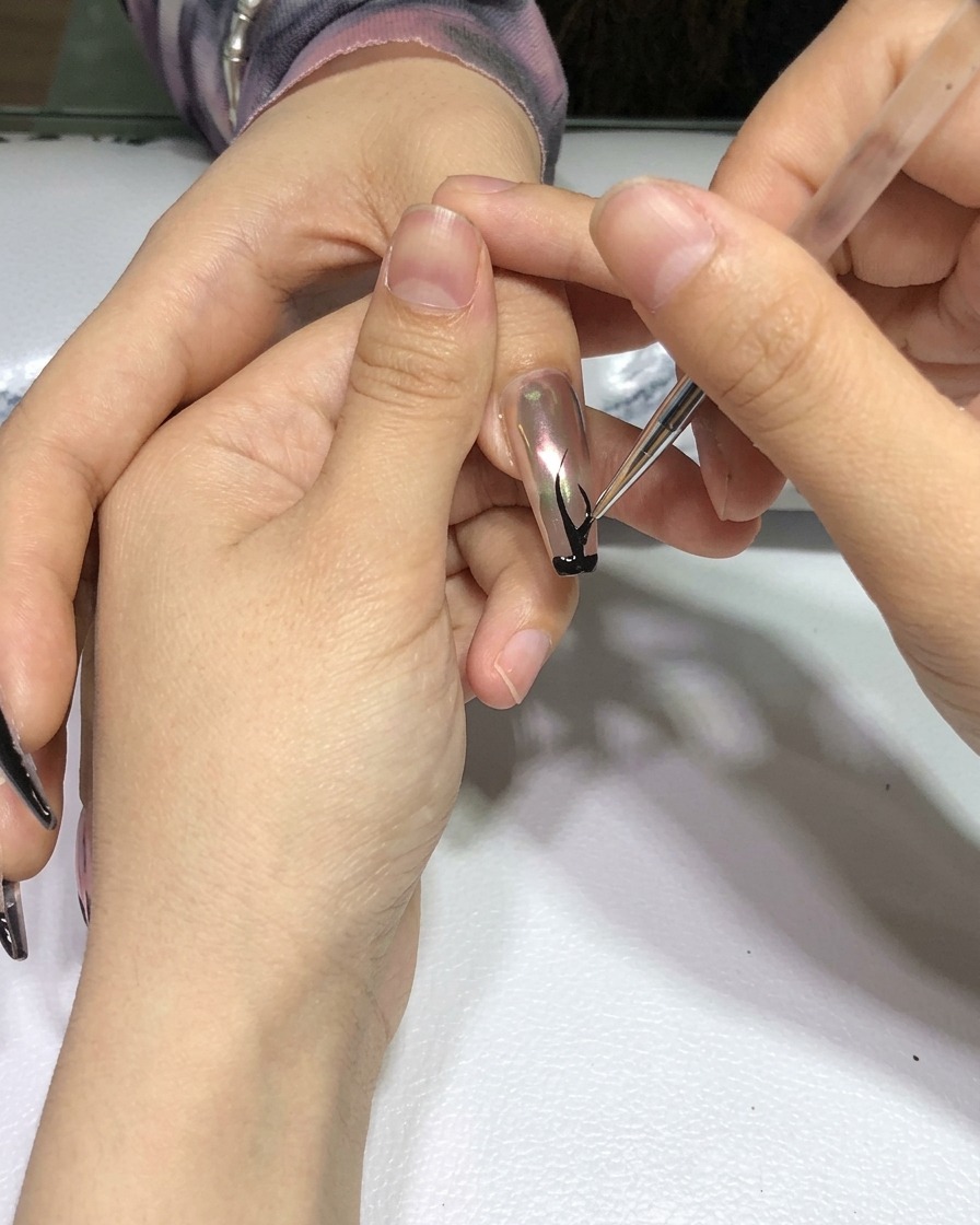 Una mano con el nail art de llamas negras terminado, colocada dentro de una lámpara de curado de uñas profesional.