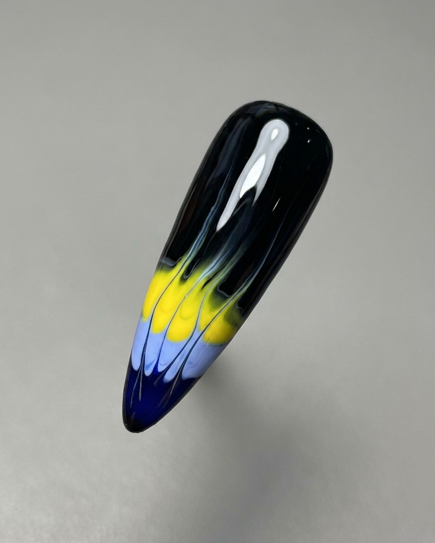 Un pincel liner fino arrastrando los geles húmedos azul y amarillo hacia arriba para crear la base del diseño de llamas.