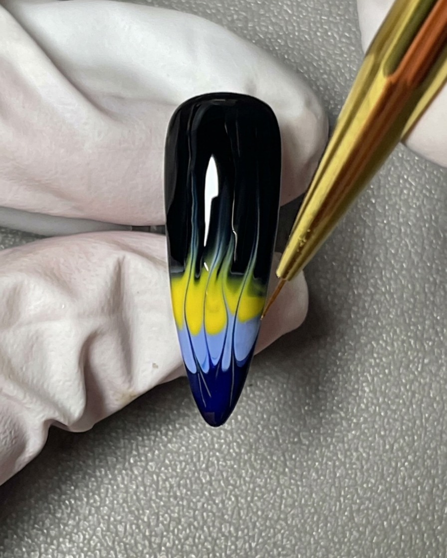 Primer plano de un pincel liner perfeccionando las puntas afiladas y alargadas del diseño de llamas sobre una uña negra.