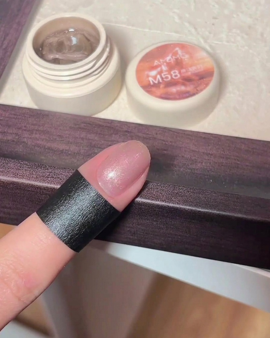 Una mano sosteniendo un imán sobre una uña con gel cat eye recién aplicado, mostrando cómo las partículas brillantes forman un patrón.