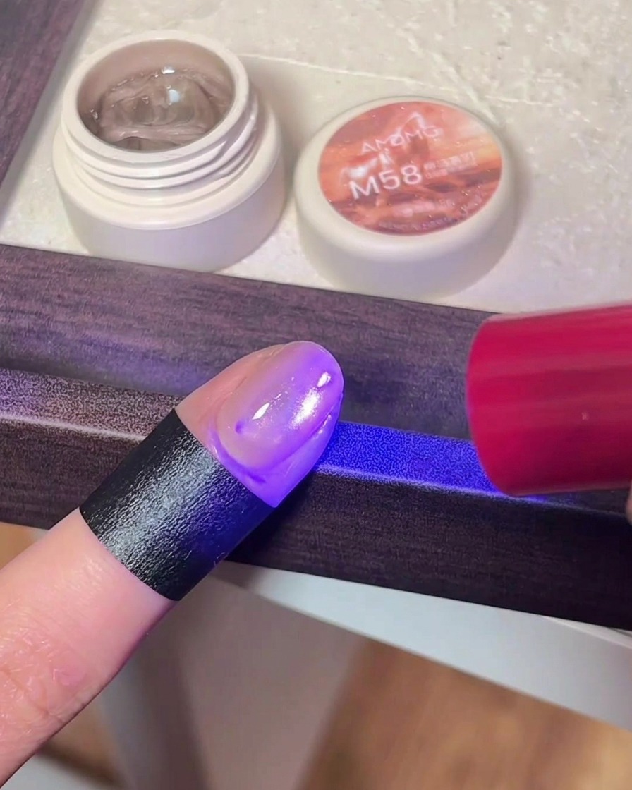 Primer plano de un dedo con esmalte cat eye bajo la luz púrpura de una lámpara UV/LED.