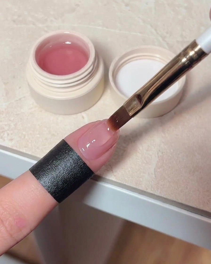 Un pincel aplicando una capa de top coat brillante sobre una uña con efecto cat eye ya curado.