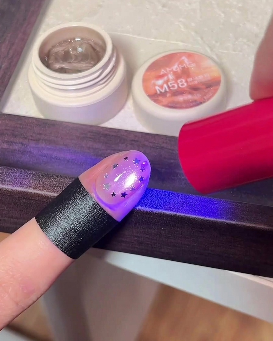 Un dedo con arte de estrellas siendo curado bajo la luz púrpura de una lámpara UV/LED.