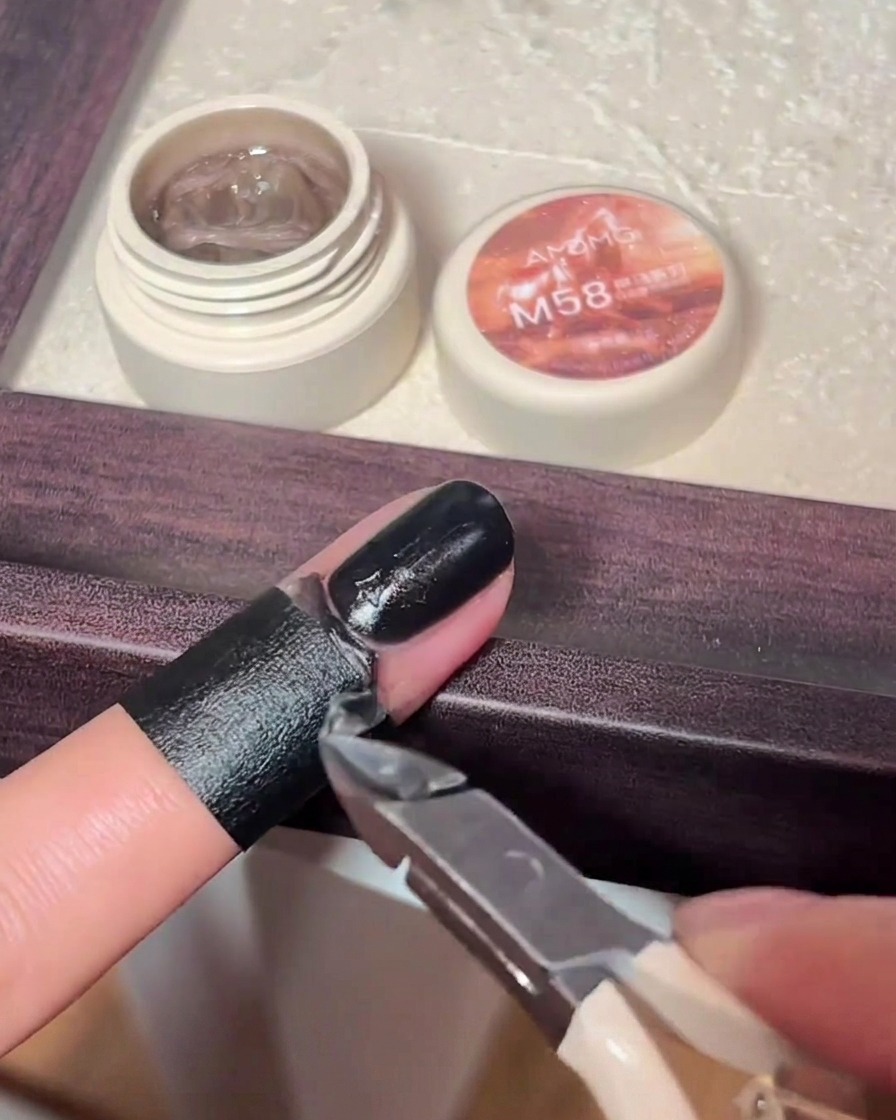 Un pequeño pincel de nail art pintando esmalte negro sobre un dije de cruz 3D en una uña.