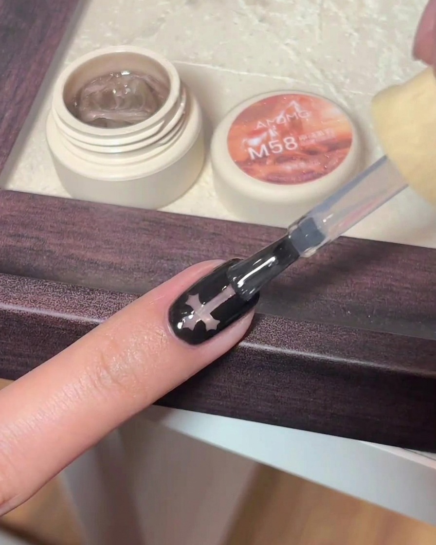 Un pincel de gel aplicando top coat brillante sobre una uña negra que presenta un diseño de cruz.