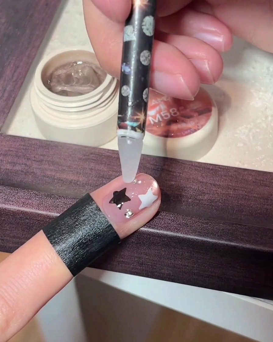 Una herramienta de precisión colocando pequeños cristales sobre una uña decorada.