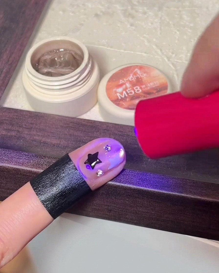Una mano curando el diseño de uñas final dentro de una lámpara LED portátil.