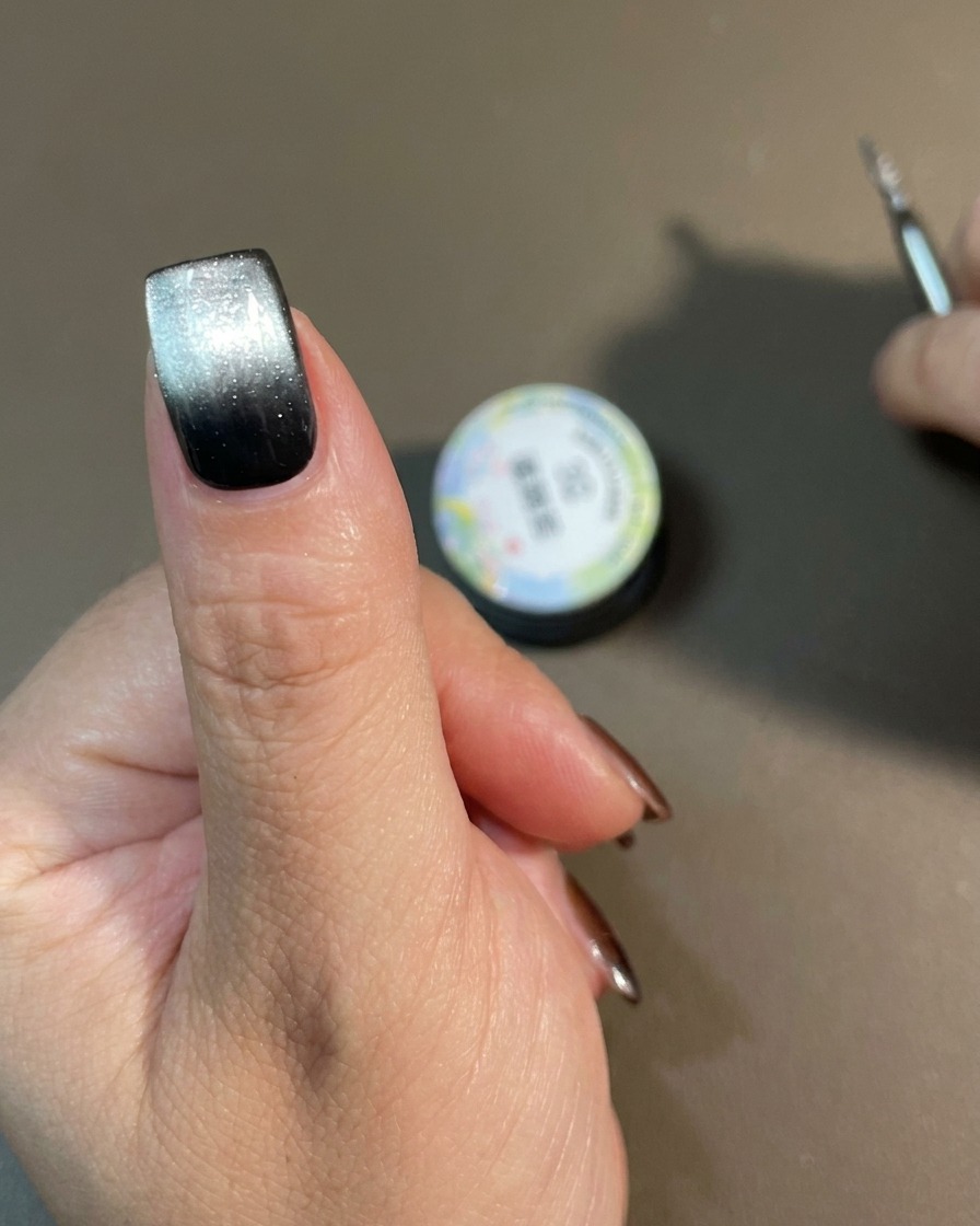 Una mano con un diseño de degradado ojo de gato terminado curándose dentro de una lámpara de uñas.